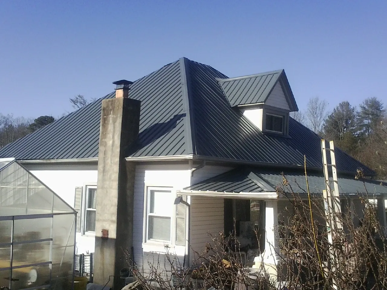 Dark blue standing seam metal roof on a white farmhouse with dormer — Slate & Tile Roof Repair by Roofing Brothers in Collettsville