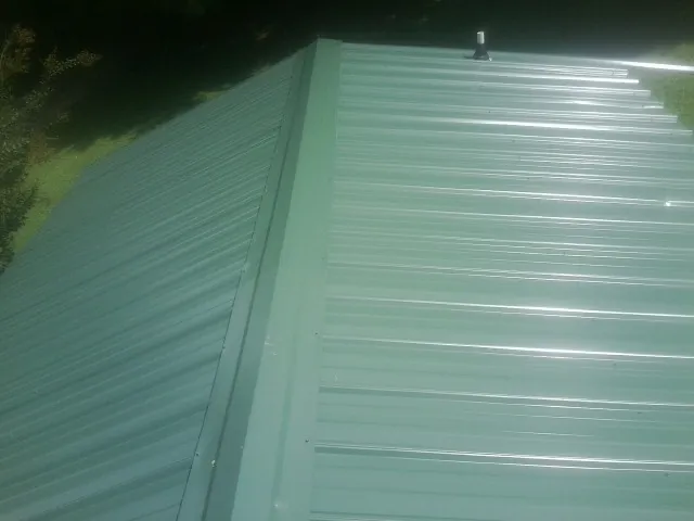 New green metal panels meeting at the ridge of a roof — Flat Roof Repair work by our crew in Collettsville
