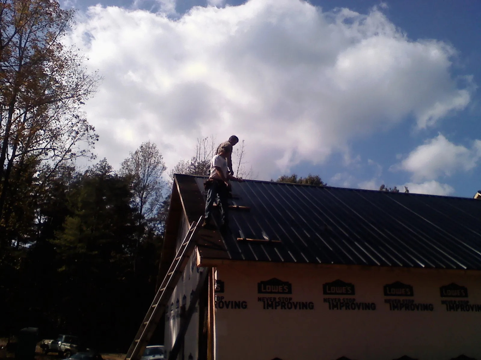Roofer fastening dark metal panels high against a cloudy sky, from a Roof Inspection job in Collettsville