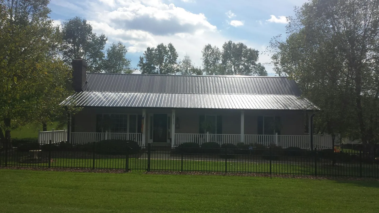Gray metal roof on a brick ranch with a full width front porch — Gutter Guard Installation work by our crew in Collettsville