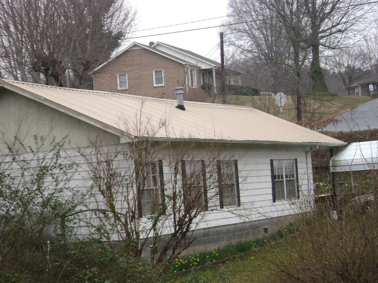 Tan metal roof on a white sided house set into a hillside — Commercial Roofing by Roofing Brothers in Collettsville