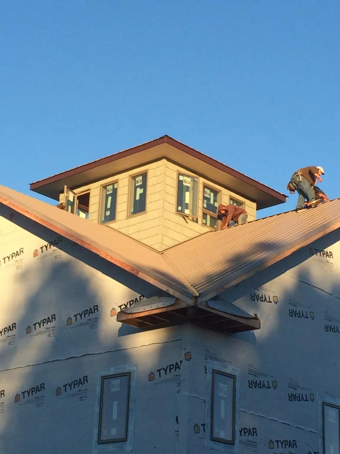 Roofers working around a rooftop cupola on a new metal roof at sunset — Roof Waterproofing in Collettsville by Roofing Brothers